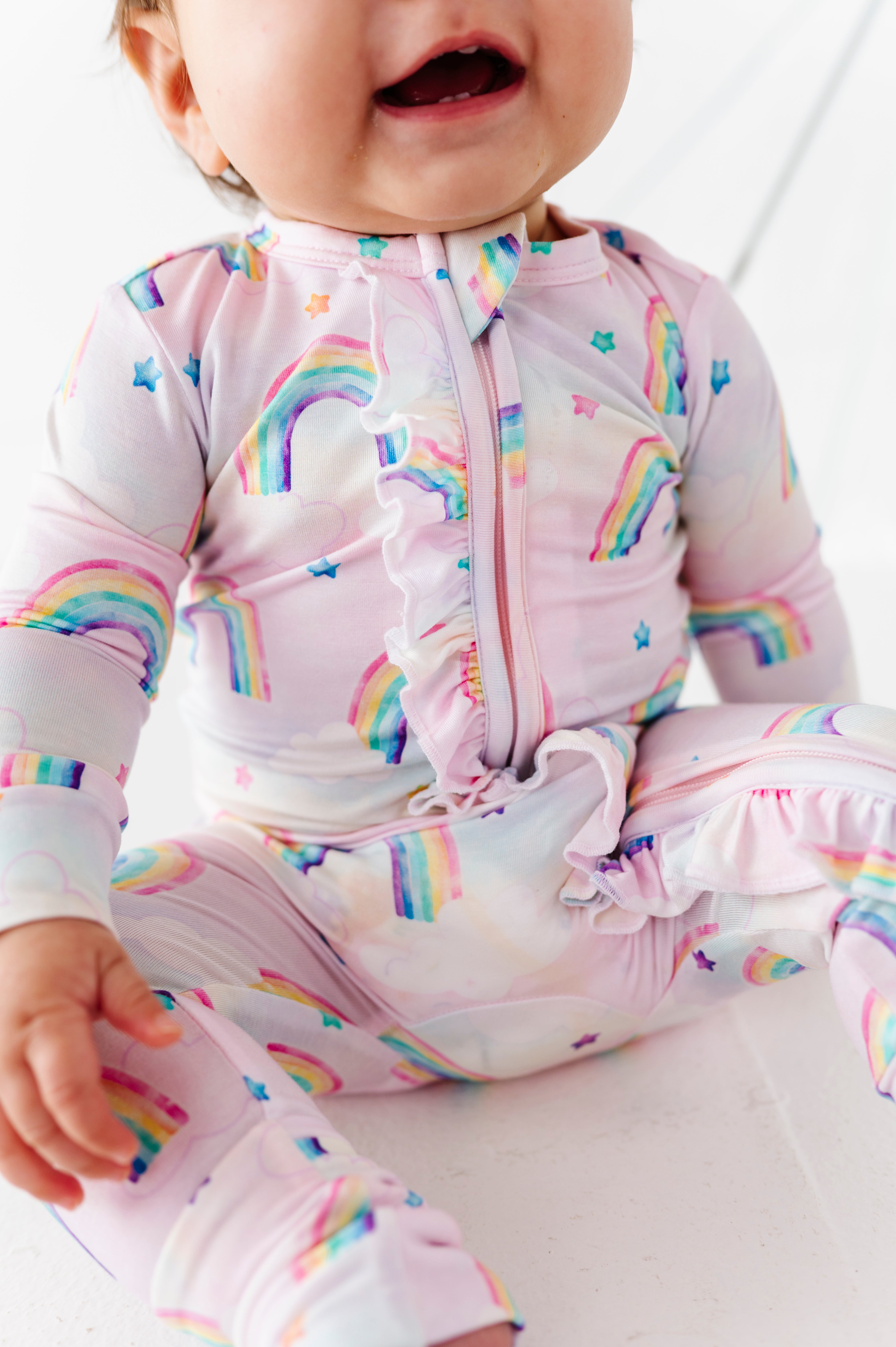 Baby wearing a pink bamboo zip romper with watercolor rainbow patterns on a white background
